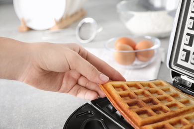 Photo of Woman taking Belgian waffles from iron on table, closeup
