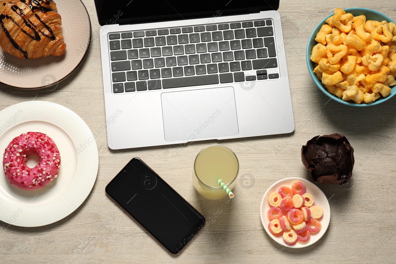 Photo of Bad eating habits at workplace. Laptop, smartphone and different snacks on wooden table, flat lay