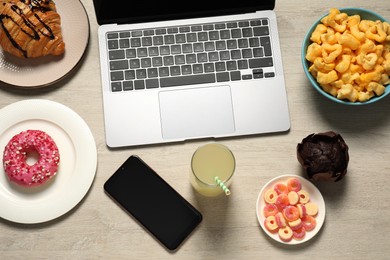 Photo of Bad eating habits at workplace. Laptop, smartphone and different snacks on wooden table, flat lay