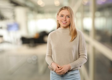 Image of Portrait of happy woman in office. Pretty girl looking at camera and smiling on blurred background, space for text