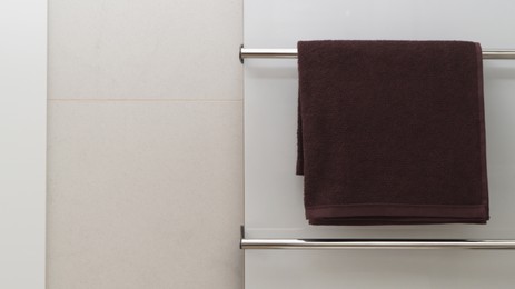 Photo of Brown soft towel on modern heated rail in bathroom, space for text