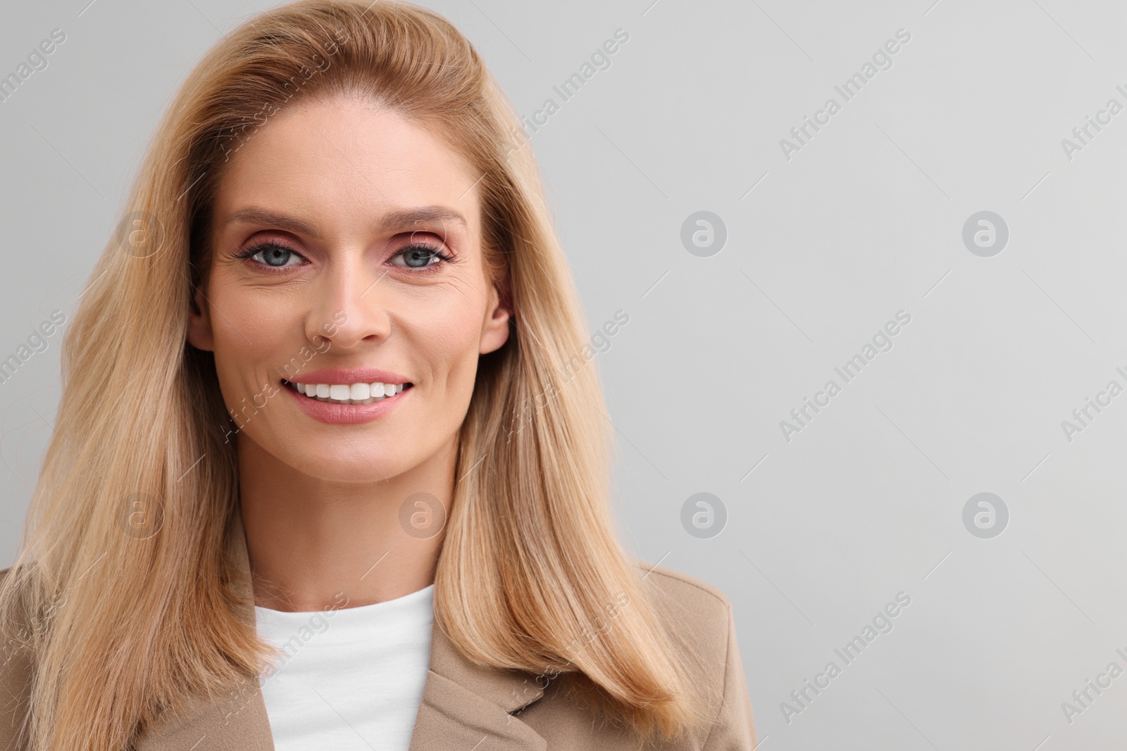 Photo of Portrait of smiling middle aged businesswoman on light grey background. Space for text
