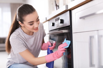 Young woman cleaning oven with rag in kitchen