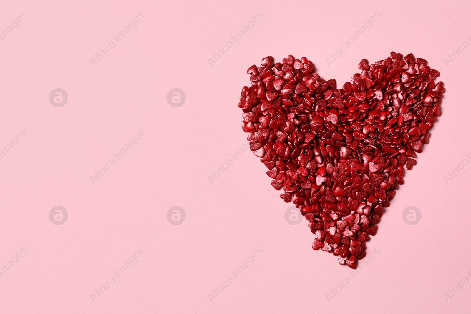 Photo of Heart made with red sprinkles on pink background, top view. Space for text