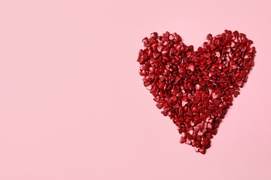 Photo of Heart made with red sprinkles on pink background, top view. Space for text