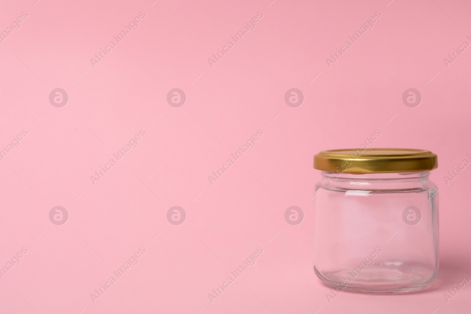 Photo of Closed empty glass jar on pink background, space for text