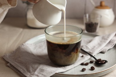 Photo of Woman pouring milk into cup with coffee at light table, closeup