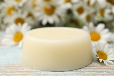 Photo of Solid shampoo bar and chamomiles on light wooden table, closeup. Hair care