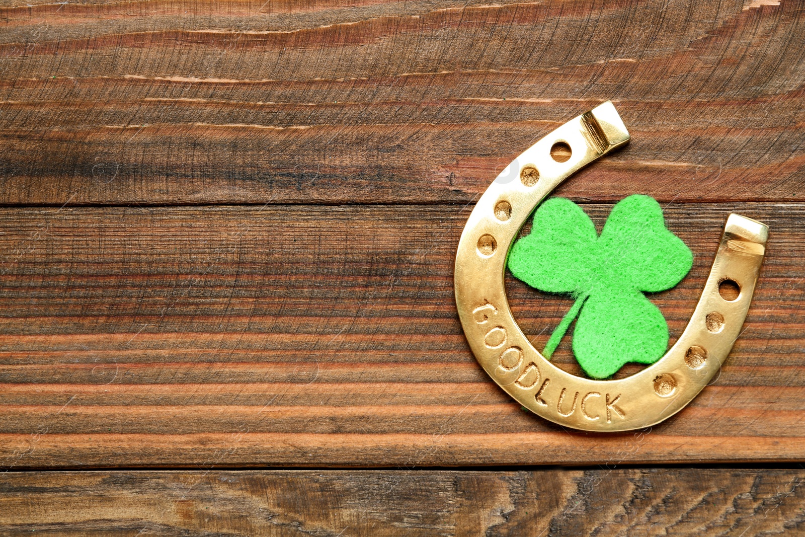 Photo of Golden horseshoe and decorative clover leaf on wooden table, flat lay with space for text. Saint Patrick's Day celebration