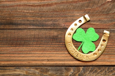 Golden horseshoe and decorative clover leaf on wooden table, flat lay with space for text. Saint Patrick's Day celebration