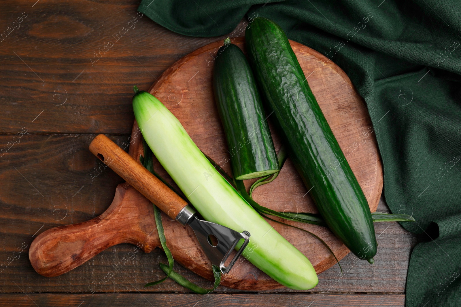 Photo of Fresh cucumbers and peeler on wooden table, top view