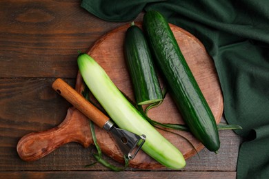 Fresh cucumbers and peeler on wooden table, top view