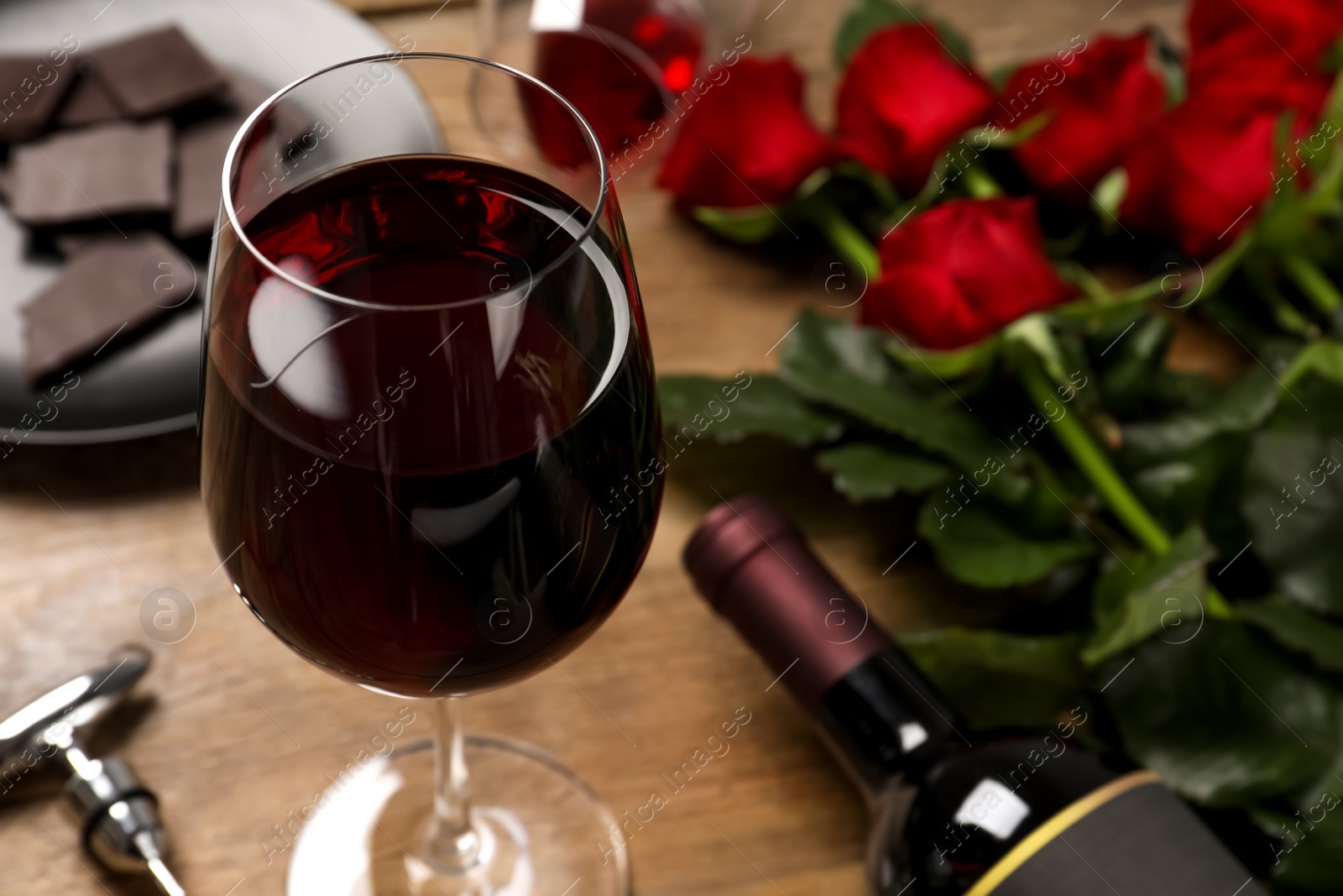 Photo of Glass of red wine near beautiful roses on wooden table, closeup