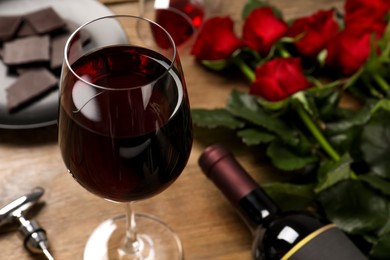 Photo of Glass of red wine near beautiful roses on wooden table, closeup