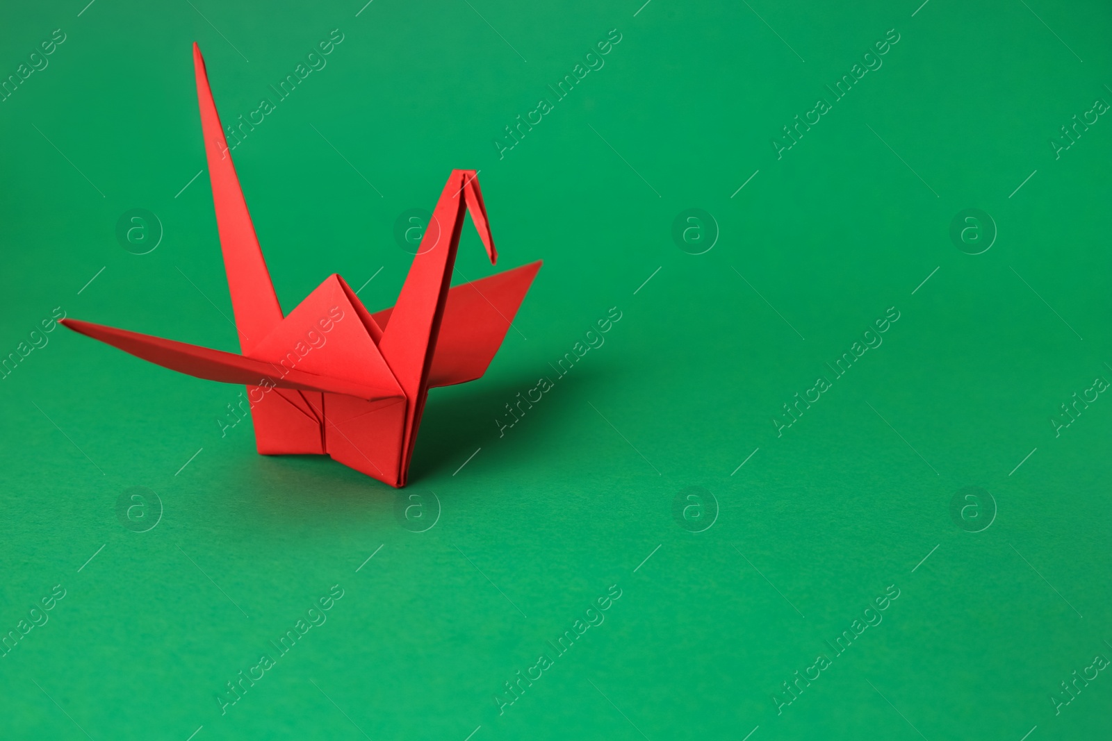 Photo of Red paper origami crane on green background, space for text