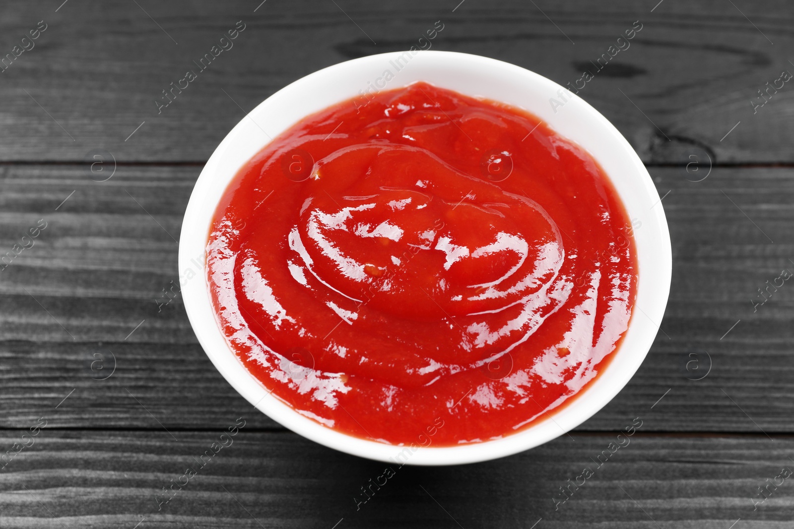 Photo of Delicious ketchup in bowl on black wooden table, above view. Tomato sauce