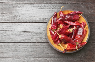 Plate with dry chili peppers on wooden background, top view