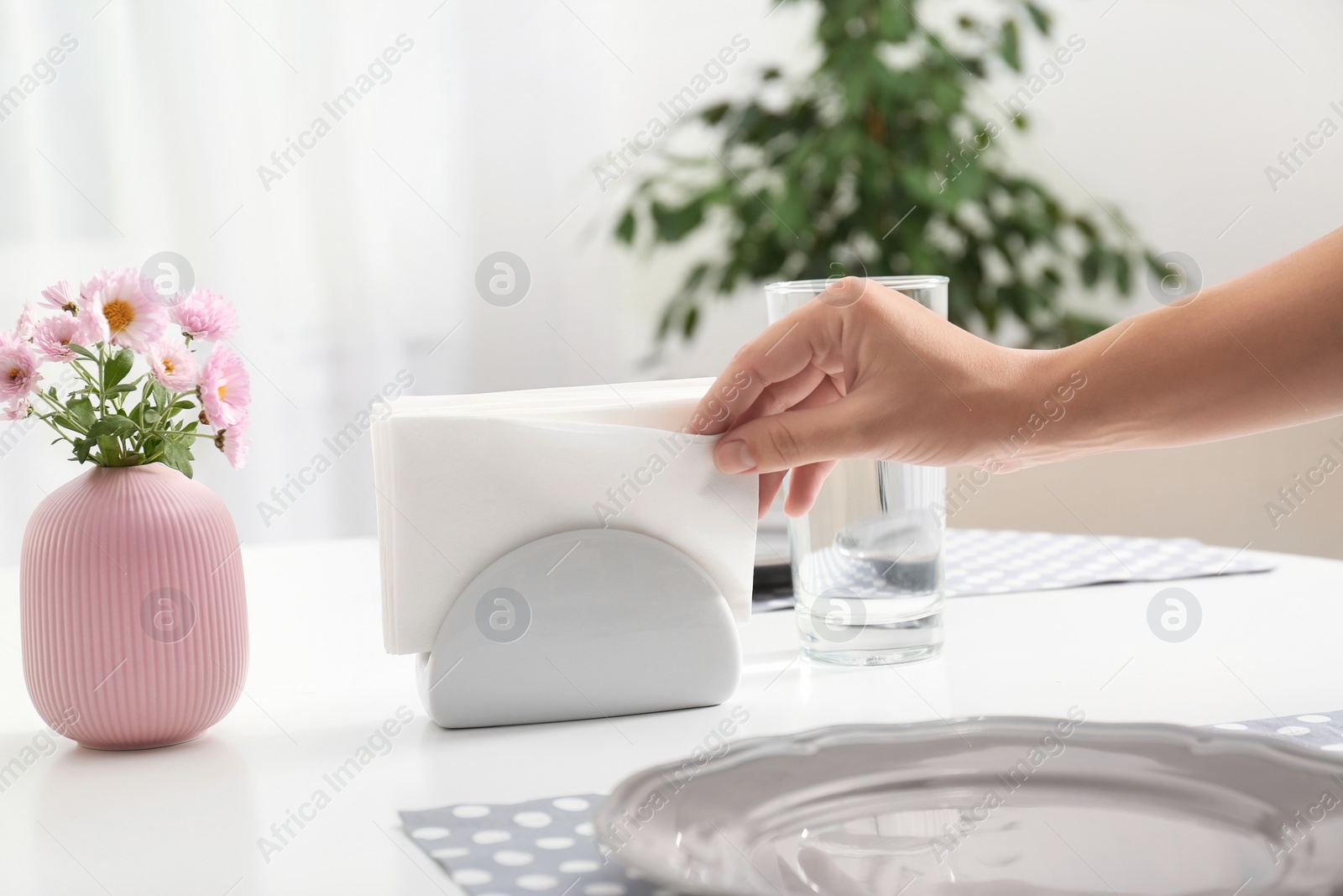 Photo of Woman taking paper tissue from ceramic napkin holder on served table