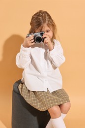 Photo of Fashion concept. Stylish girl with vintage camera on pale orange background