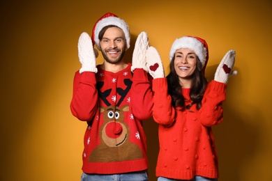 Young couple in Christmas sweaters and hats on yellow background