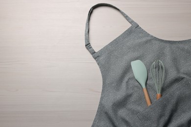 Stylish apron, spatula and whisk on white wooden table, top view. Space for text