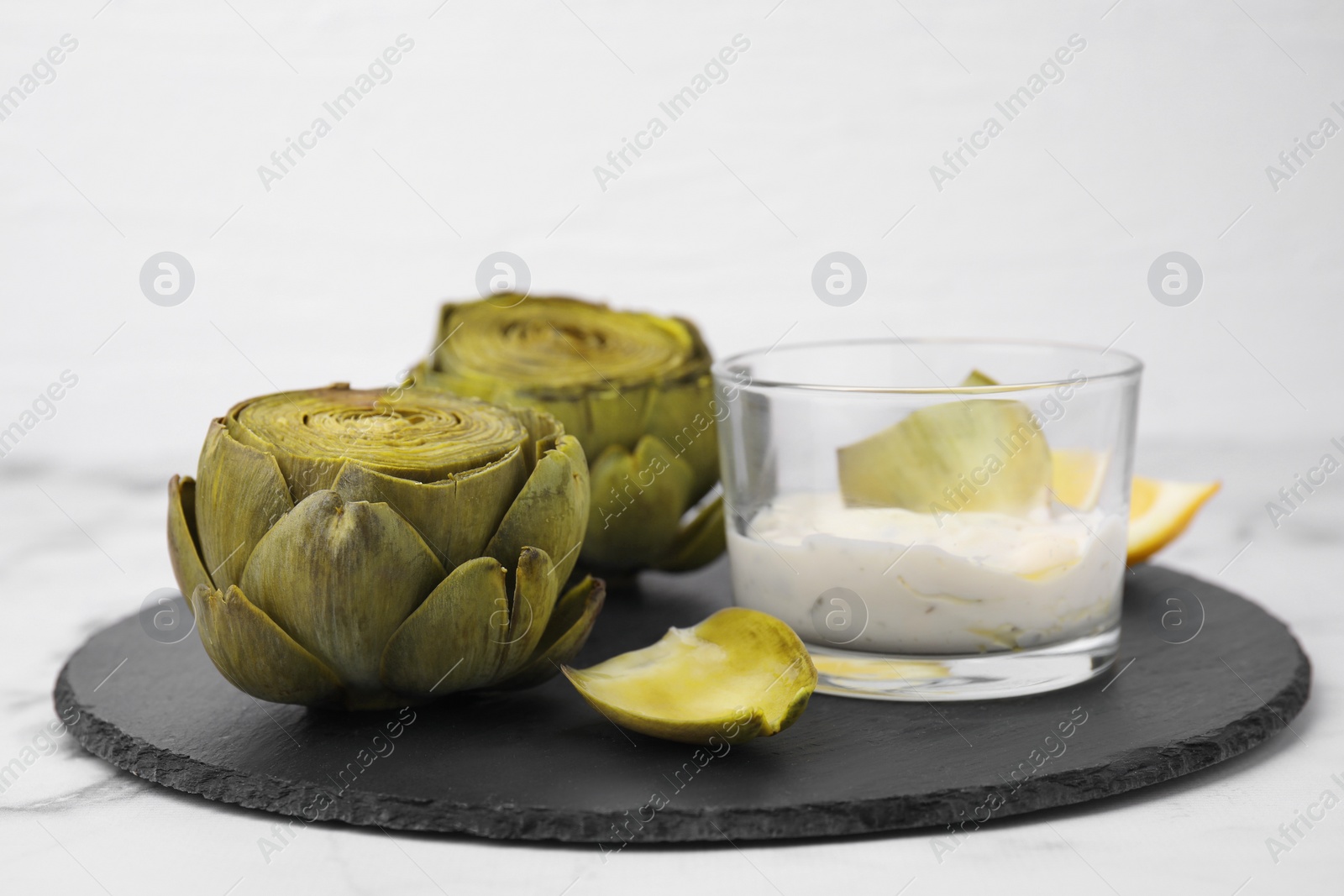 Photo of Delicious cooked artichokes with tasty sauce served on white table, closeup