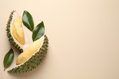 Photo of Pieces of fresh ripe durian and leaves on beige background, flat lay. Space for text