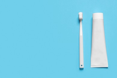 Photo of Plastic toothbrush with paste and tube on light blue background, flat lay. Space for text