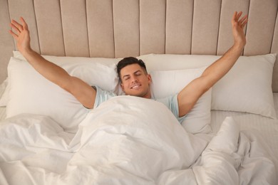 Man stretching in bed with white linens at home