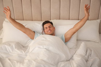 Photo of Man stretching in bed with white linens at home