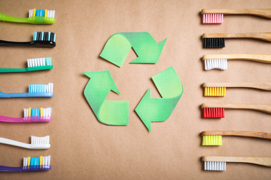 Photo of Recycling symbol, plastic and bamboo toothbrushes on beige background, flat lay