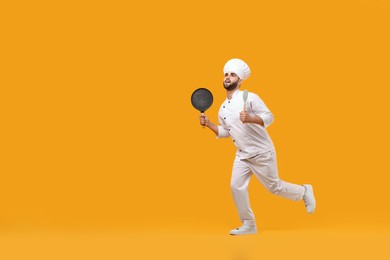 Photo of Professional chef with pan and spatula having fun on yellow background