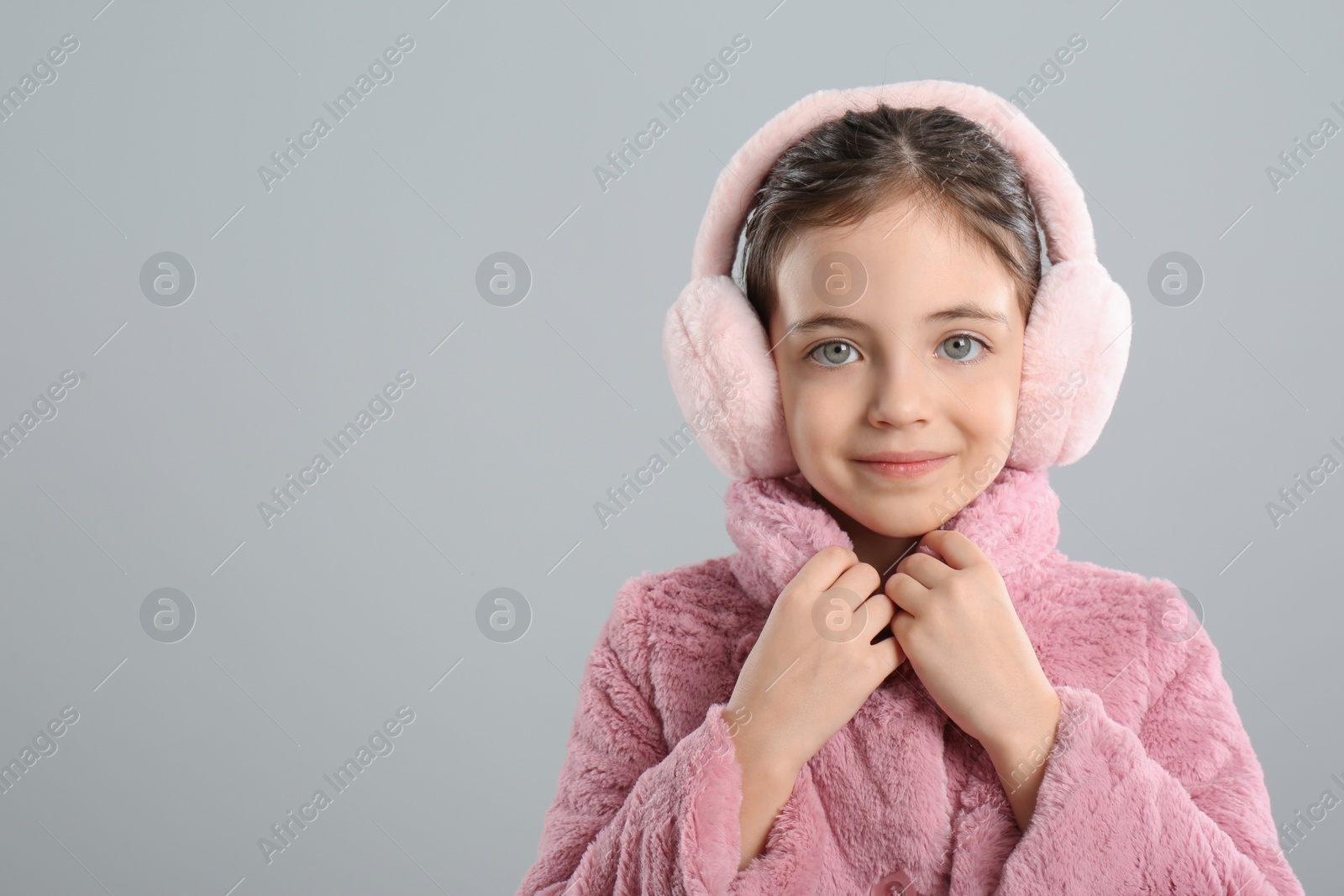 Photo of Cute girl wearing stylish earmuffs on grey background. Space for text