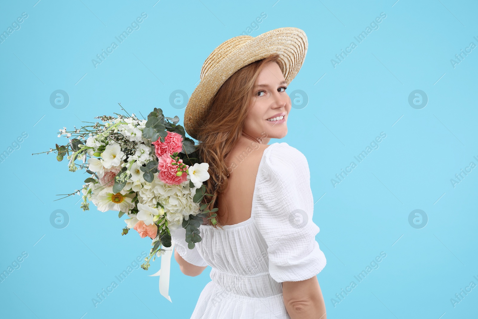 Photo of Beautiful woman in straw hat with bouquet of flowers on light blue background