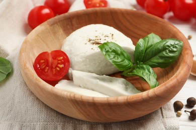 Delicious mozzarella with tomato and basil leaves in wooden bowl on table, closeup