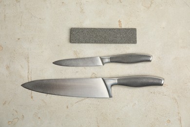 Photo of Sharpening stone and knives on grey table, flat lay