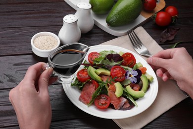 Woman adding soy sauce to tasty salad at wooden table, closeup