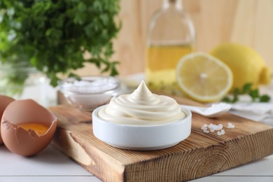 Photo of Fresh mayonnaise sauce in bowl and ingredients on white wooden table