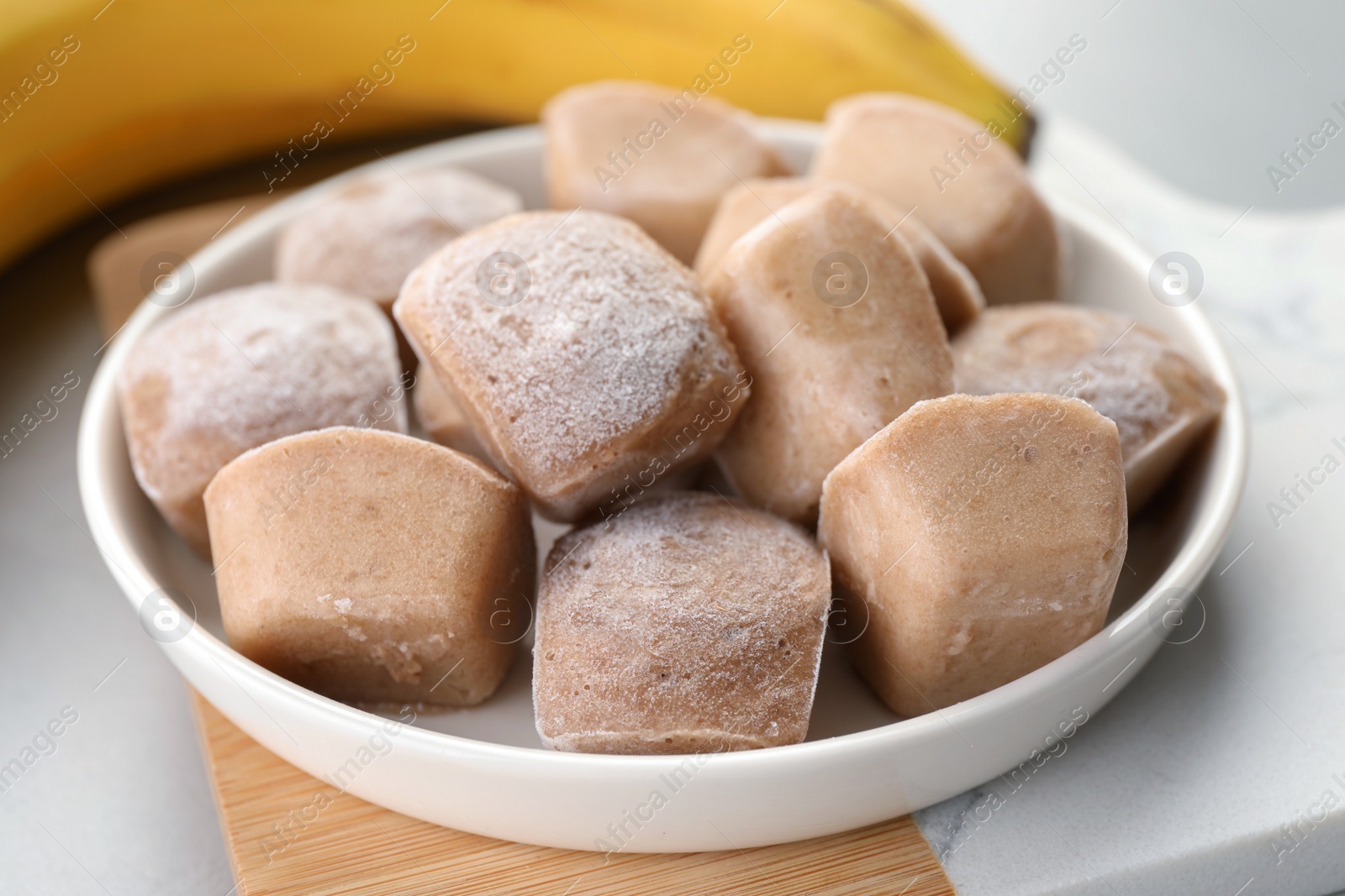 Photo of Frozen banana puree cubes and ingredient on light grey table, closeup