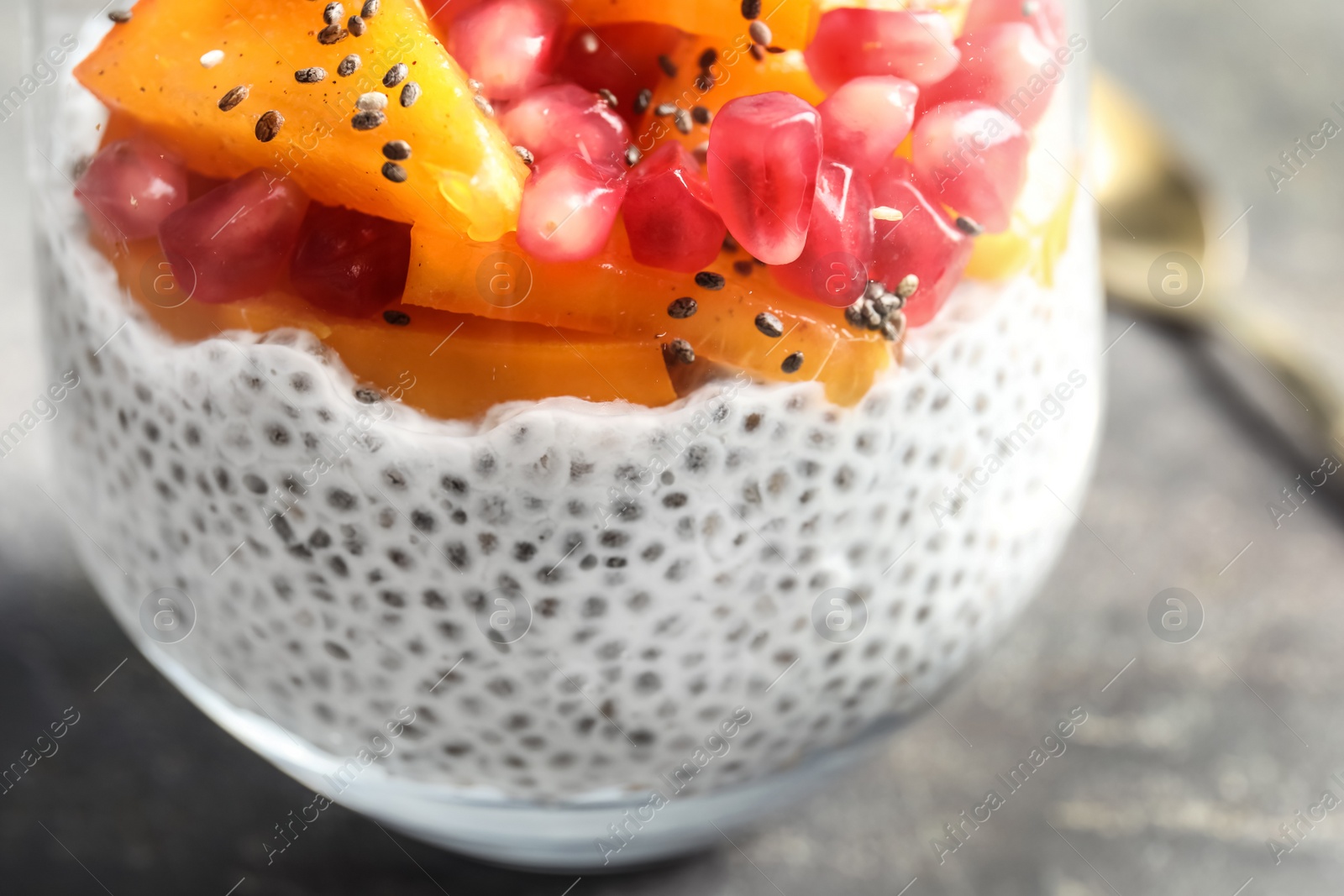 Photo of Glass of tasty chia seed pudding with persimmon and pomegranate on table, closeup