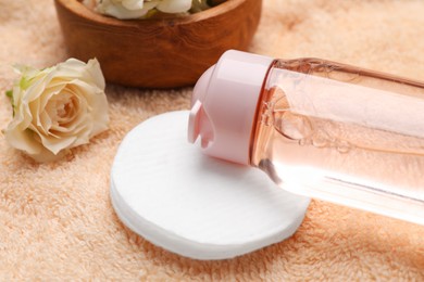 Photo of Bottle of micellar cleansing water, cotton pads and flowers on pink towel, closeup