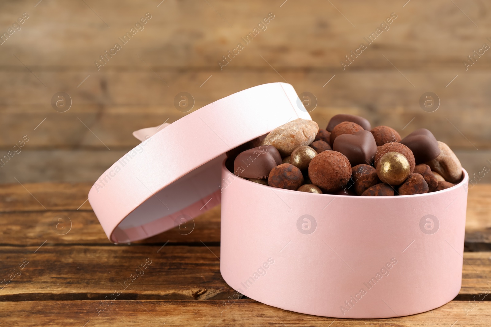 Photo of Different delicious chocolate candies in box on wooden table