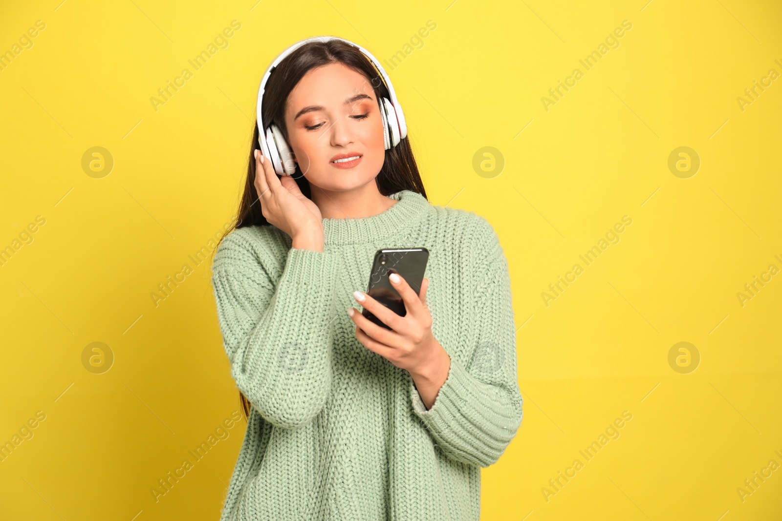 Photo of Young woman listening to audiobook on yellow background