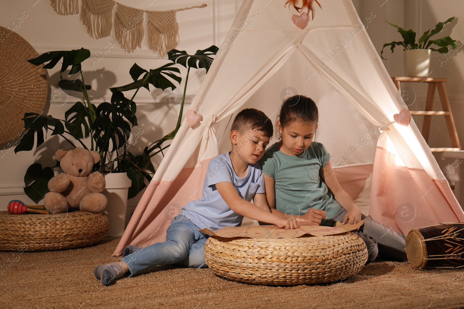 Photo of Cute little children with treasure map near toy wigwam at home