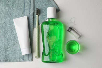 Fresh mouthwash in bottle, glass, toothbrush, toothpaste and dental floss on light background, flat lay