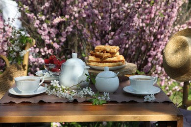 Photo of Beautiful spring flowers, freshly baked waffles and ripe strawberries on table served for tea drinking in garden