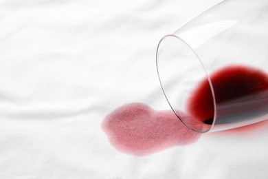 Photo of Overturned glass and spilled exquisite red wine on white t-shirt. Space for text