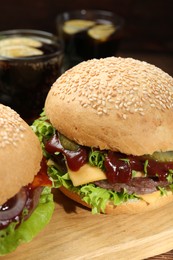 Photo of Wooden board with delicious cheeseburgers against blurred background, closeup