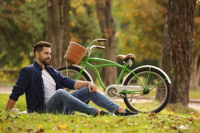 Photo of Young man sitting on green grass near bicycle in park