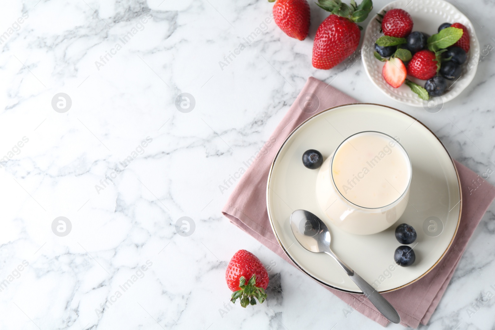 Photo of Tasty yogurt in glass and berries on white marble table, flat lay. Space for text